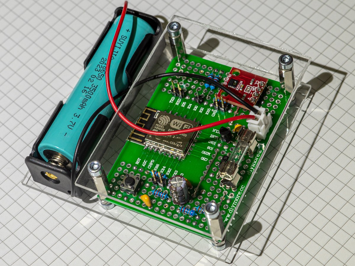 The assembled ESPtemp board with an ESP8266 and an HTU21D sensor in an acrylic case, next to its 18650 cell